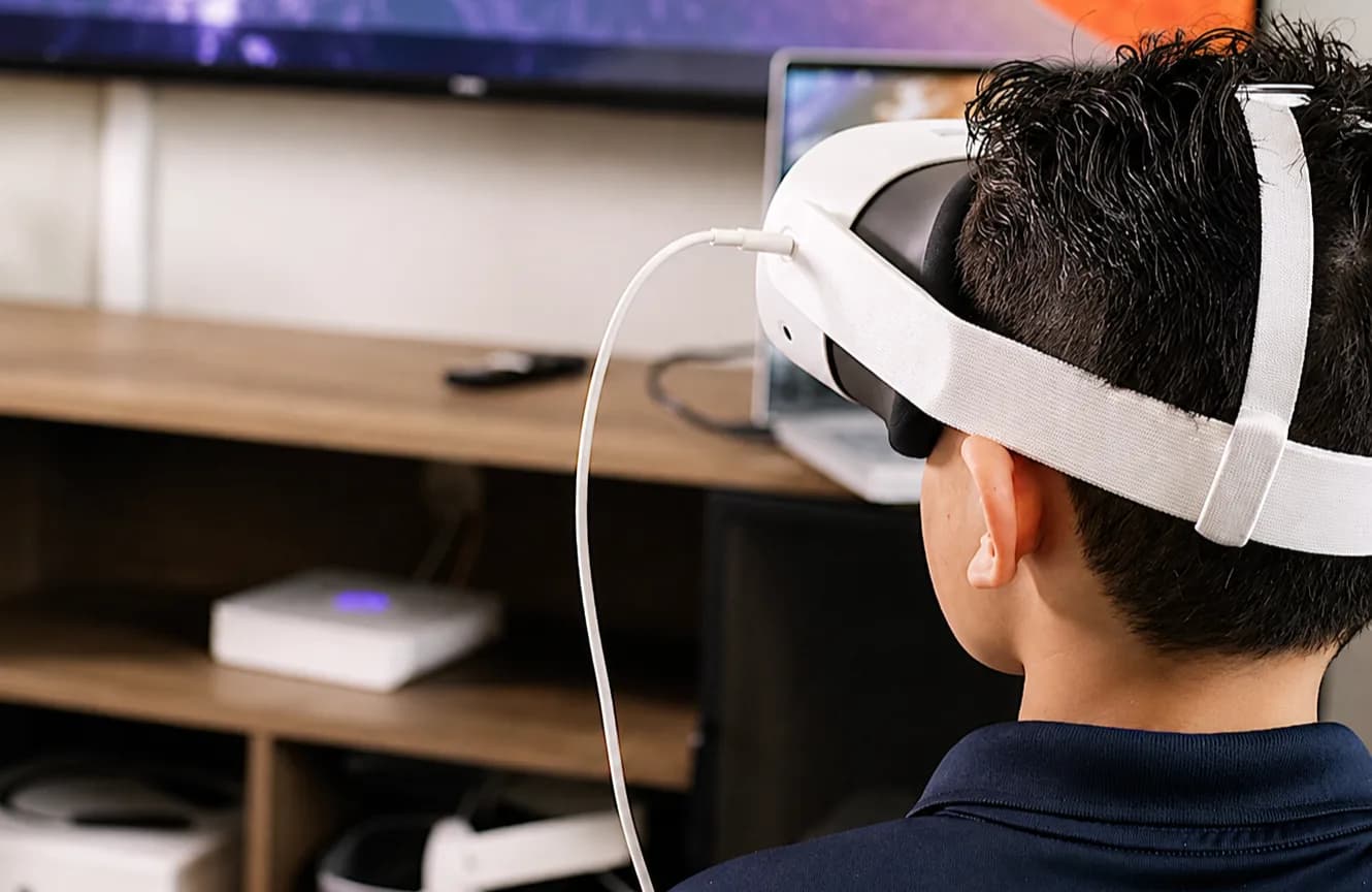A student at home in a VR headset, a space scene on the screen in front of them.