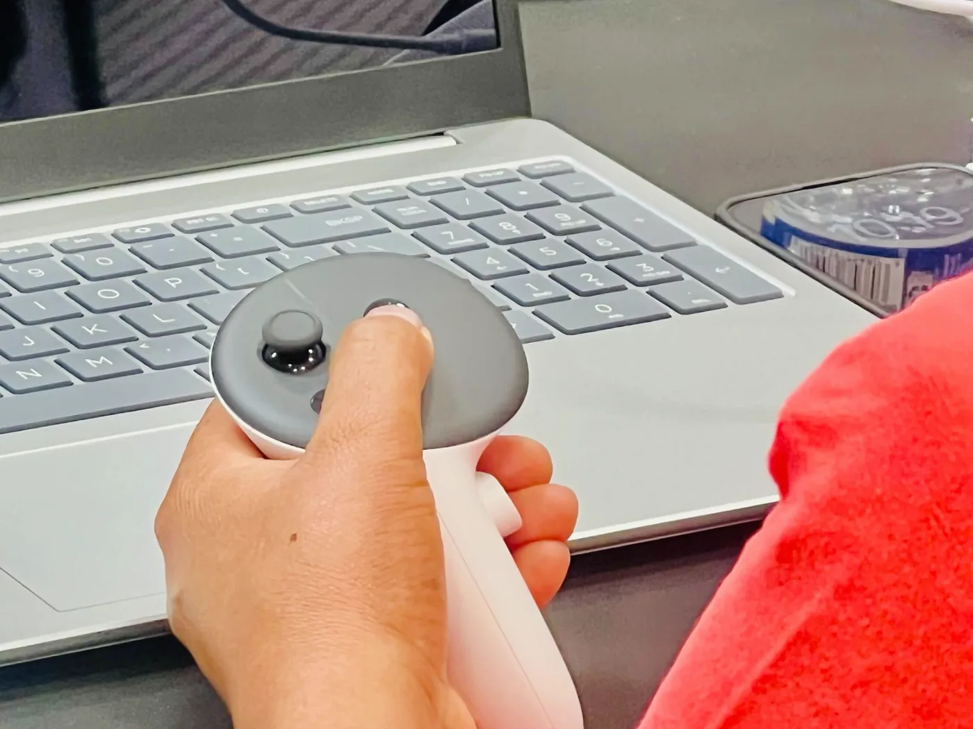 A student holds a VR controller beside an open laptop.