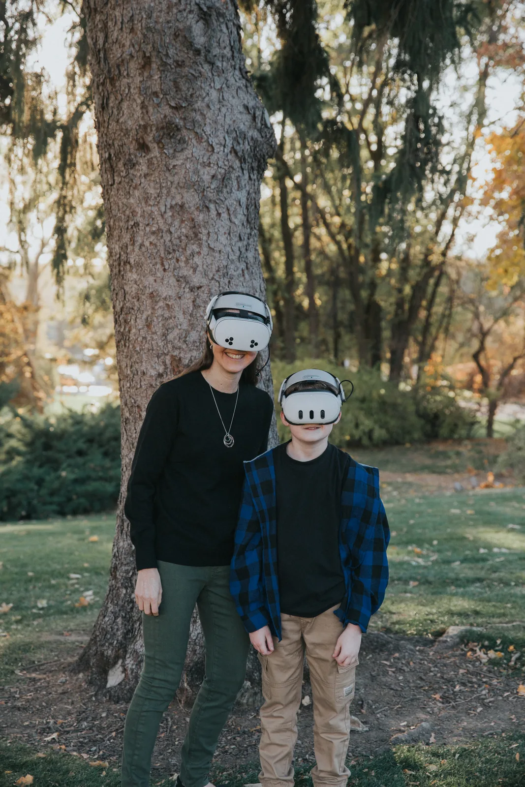 Tiffany Strong and her younger son stand beside a tree outdoors, both wearing virtual reality headsets.